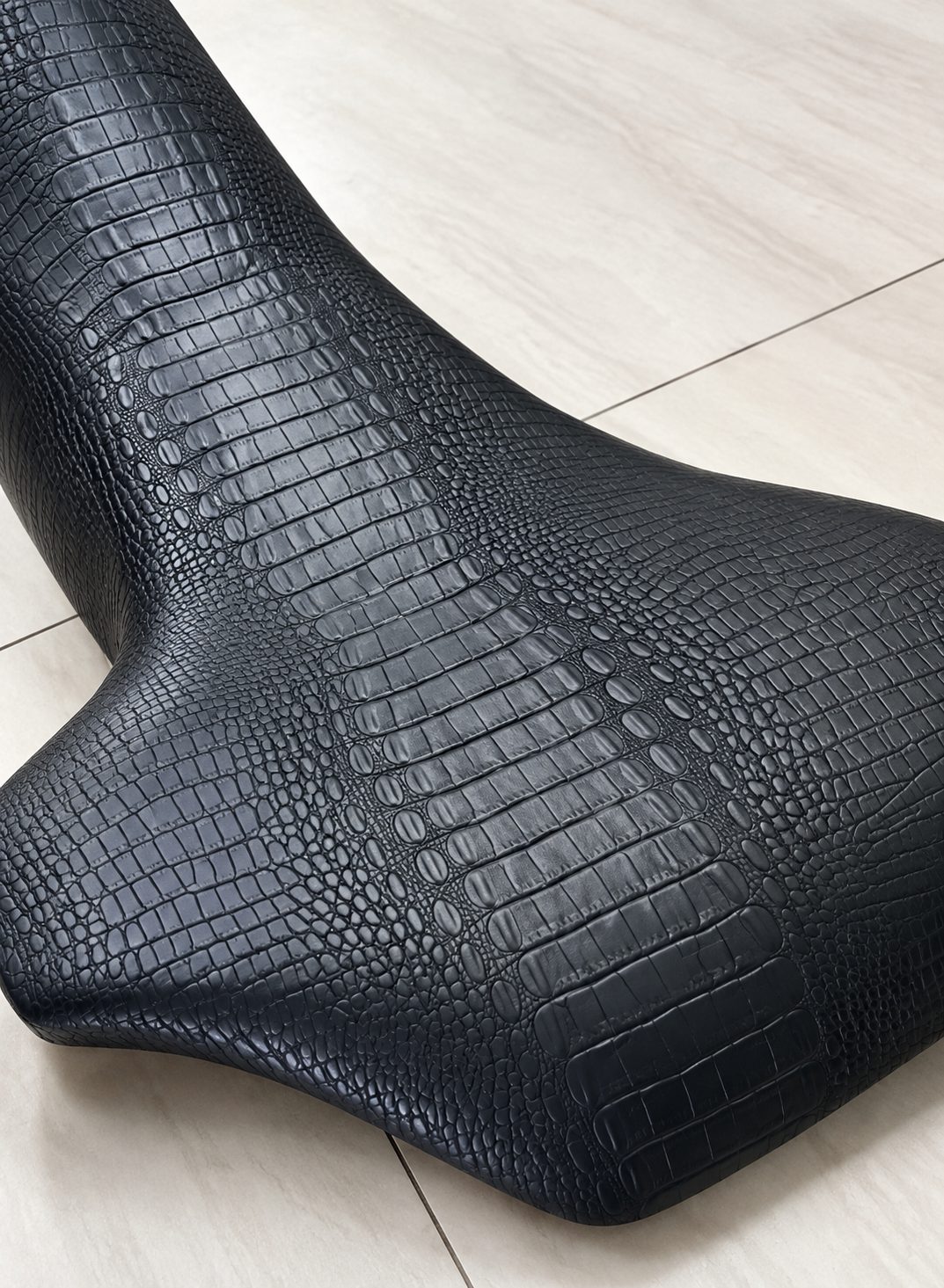 Motorcycle seat upholstered in black crocodile-textured material.