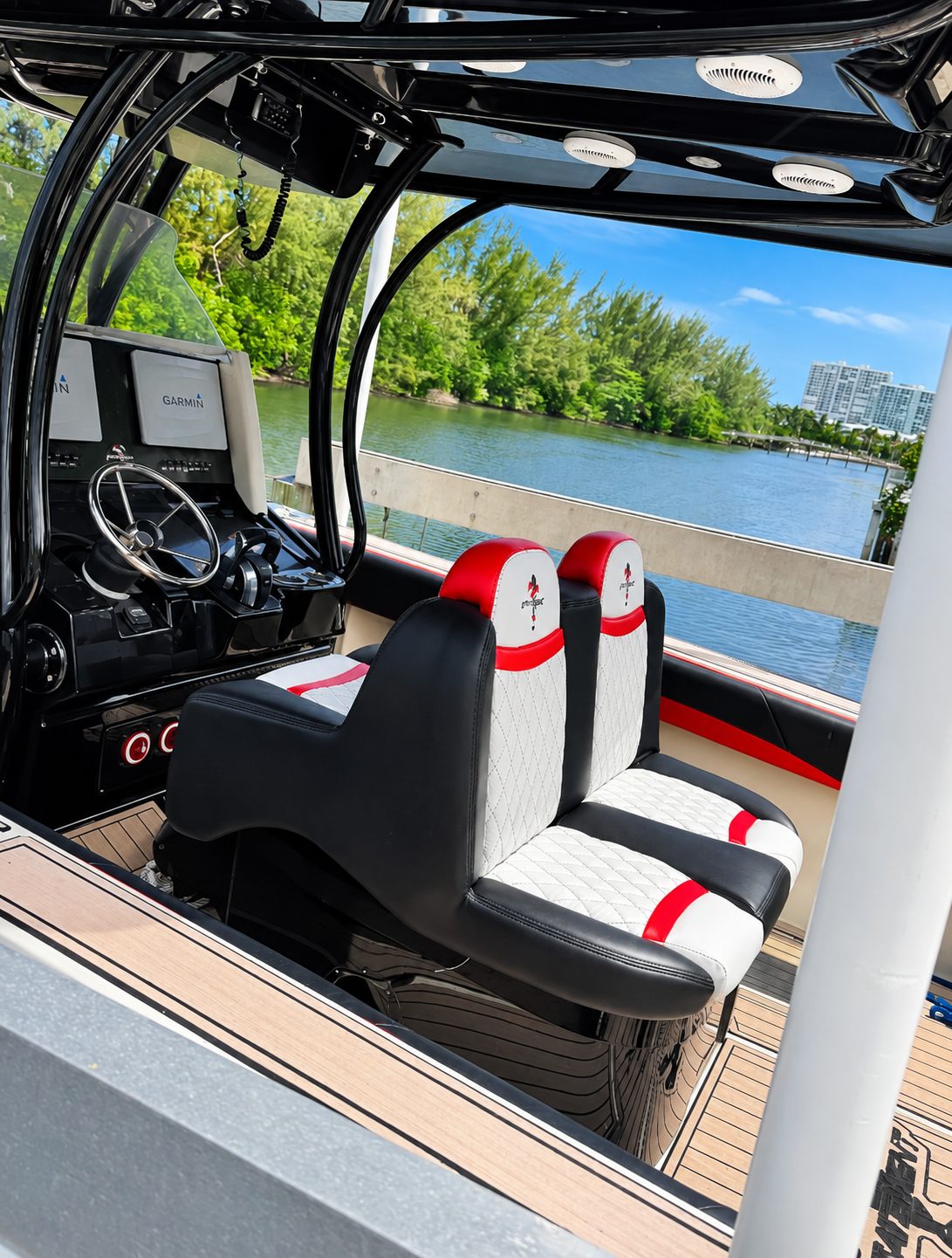 Side view of the black, white and red diamond-stitched helm seats beside the console of a boat on the water.