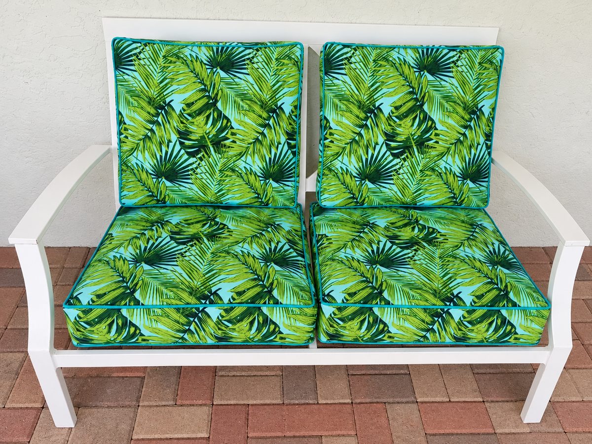Green tropical-print seat and back cushions on a white patio bench.