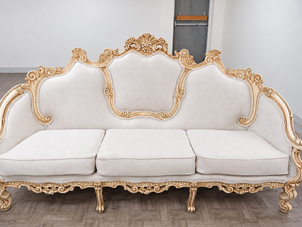 White upholstered sofa with an ornate ivory-and-gold frame in a workshop.