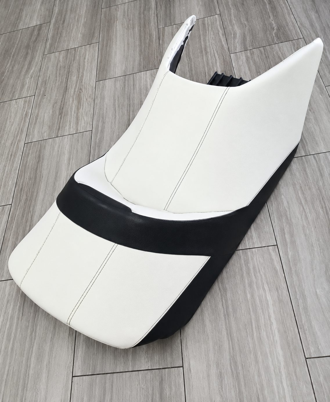 Custom motorcycle seat upholstered in white with black side panels and contrast stitching.